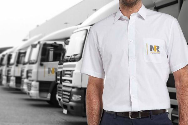 Man wearing NRI Branded Short Sleeved Shirt in front of trucks